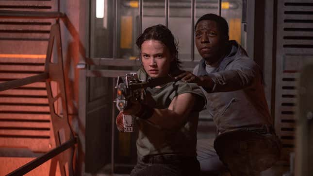 Rain wields a gun while Andy stands behind her.